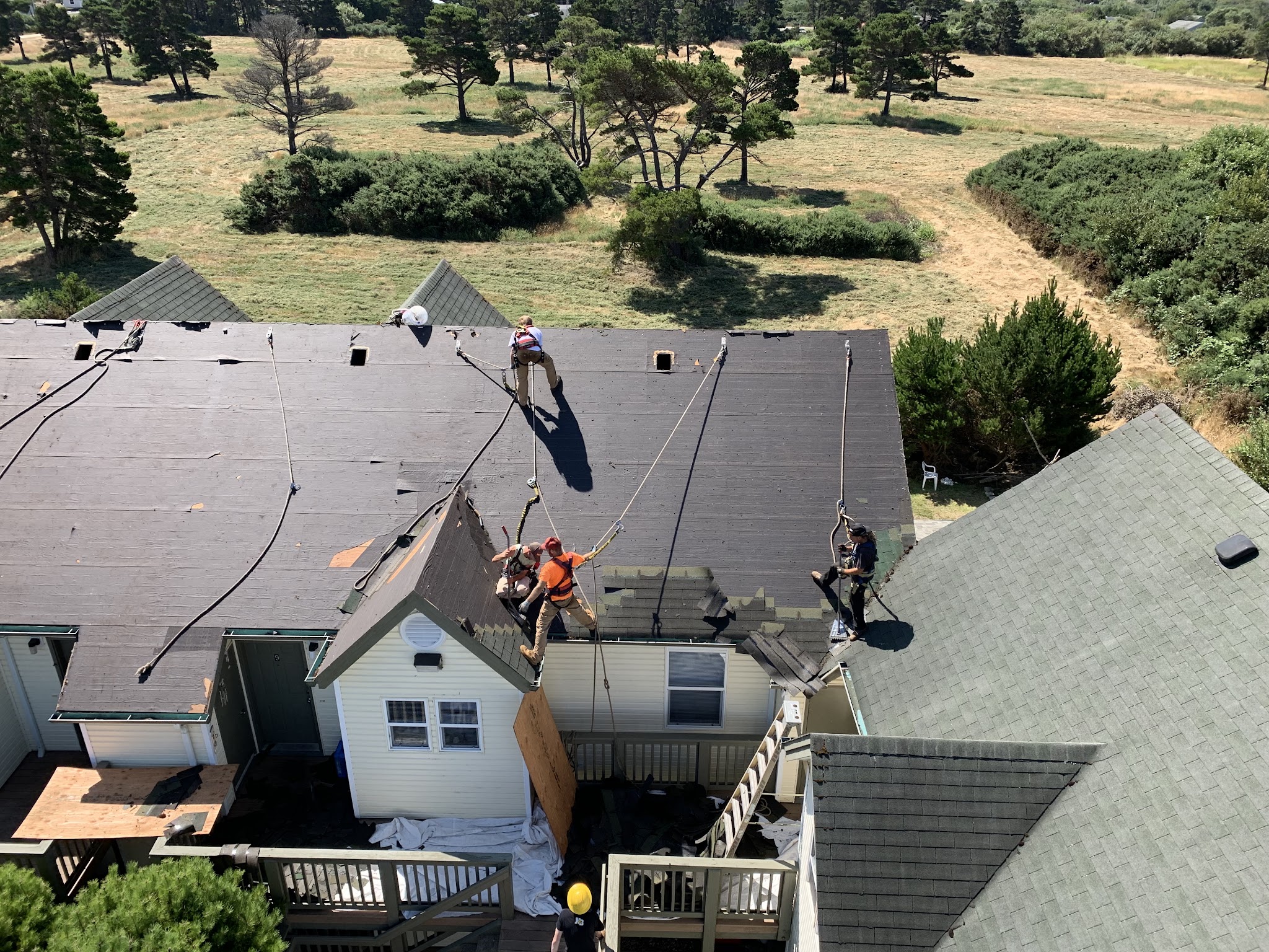 Crew roped off and working across a multi-gable coastal roof during a full reroof